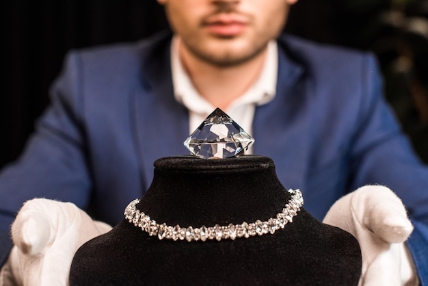 Przycięty widok rzeczoznawcy biżuterii trzymającego stojak na naszyjnik z naszyjnikiem i kamieniem szlachetnym na czarno