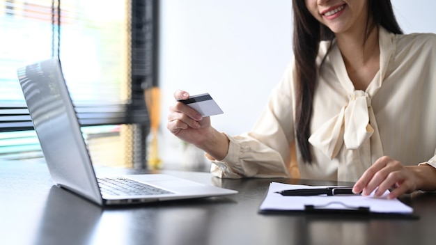 Przycięty widok uśmiechniętej młodej kobiety trzymającej kartę kredytową i używającej laptopa Koncepcja e-commerce zakupów online
