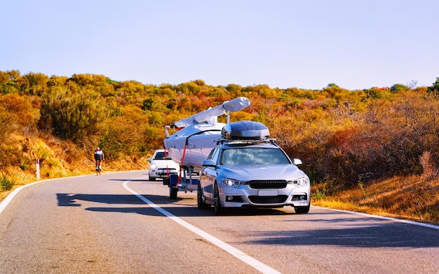 Przyczepa Samochodowa Z Jachtem Lub Motorówką Na Drodze Na Costa Smeralda Na Wyspie Sardynia, Włochy Lato. Minivan Z Motorówką Na Autostradzie Na Wakacjach Na Autostradzie. Prowincja Olbia. Różne środki Przekazu.