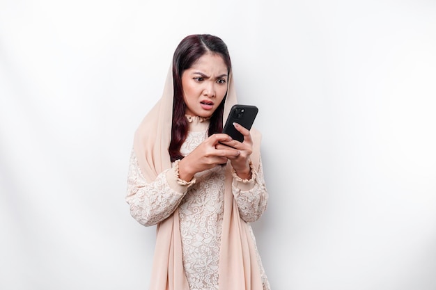 Przygnębiająca azjatycka muzułmanka w chustce na głowie wygląda na zestresowaną podczas rozmowy przez telefon odizolowanej białym tłem