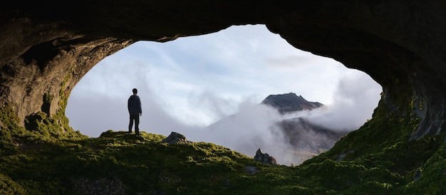 Przygód mężczyzna stojący w skalistej jaskini Górski krajobraz przyrody z chmurami w tle