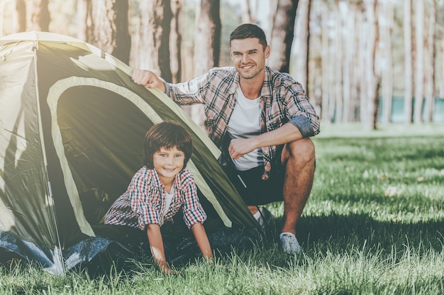 Przygoda poza domem. Wesoły ojciec i syn siedzą w pobliżu namiotu podczas biwakowania w lesie