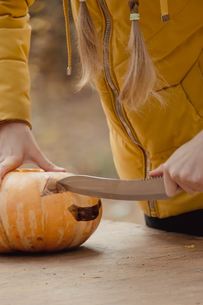 Zdjęcie przygotowanie do halloween: dziewczyna krojąca dynię. zbliżenie. koncepcja dekoracji wakacje. kobieta przygotowuje jack-o-latarnia. impreza dekoracyjna. mały pomocnik.