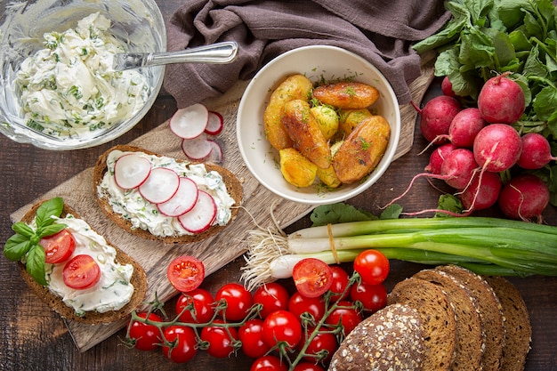 Zdjęcie przygotowanie letnich kanapek z twarogiem z zieloną cebulą, rzodkiewką i pomidorami. dieta ketonowa, ziemniaki smażone w całości.