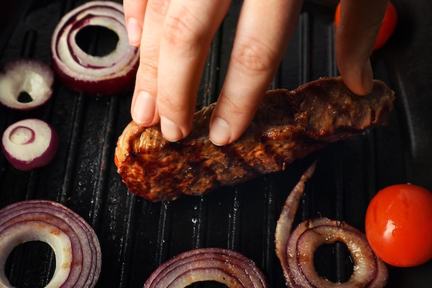 Przygotowanie steku z pierścieniami cebuli i pomidorami na patelni grill closeup