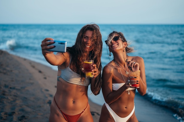 Przyjaciele cieszą się razem wakacjami i robią sobie selfie na plaży za pomocą smartfona