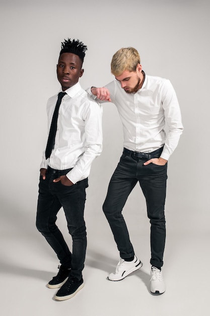 Przyjaciele dwóch facetów w białych koszulach i ciemnych spodniach pozują w studio na białym tle