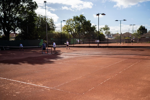 Przyjaciele grają w tenisa na boisku glinianym, podlewają i workują boisko gliniane, utrzymują boisko tenisowe.