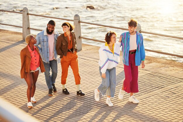 Zdjęcie przyjaciele morze i różnorodność z ludźmi spacerującymi razem po promenadzie latem z góry szczęśliwy uśmiech i ocean z grupą przyjaciół mężczyzny i kobiety łączącą się podczas spaceru na zewnątrz przy plaży