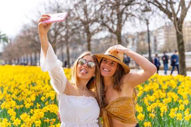 Przyjaciele na wakacjach w mieście w słomkowych kapeluszach obok pięknych żółtych kwiatów dużo się uśmiechają i cieszą się wiosną robiąc selfie