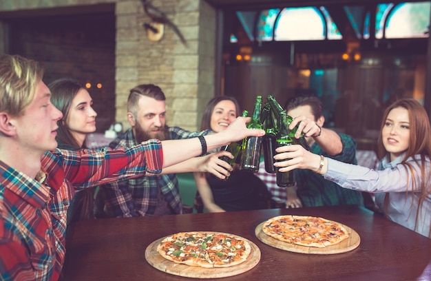 Przyjaciele Piją Drinki W Barze, Siedzą Przy Drewnianym Stole Z Piwem I Pizzą.