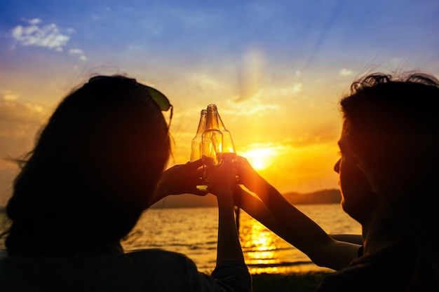 Zdjęcie przyjaciele podnoszą butelki piwa na jeziorze podczas zachodu słońca