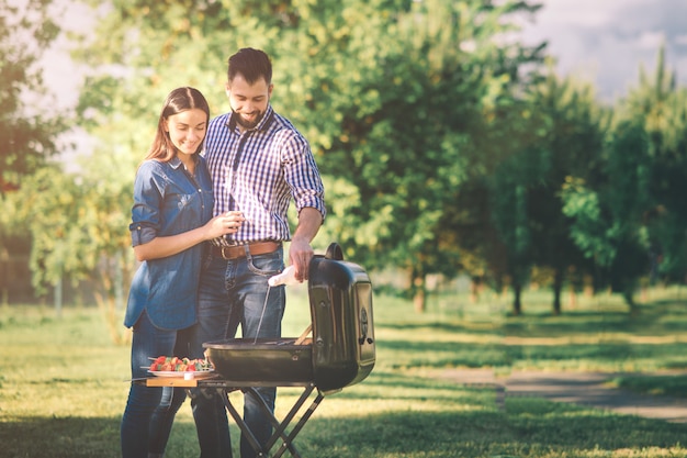 Przyjaciele Robi Grilla I Je Lunch W Naturze. Para Zabawy Podczas Jedzenia I Picia W Pic-nic - Szczęśliwi Ludzie Na Imprezie Z Grilla.