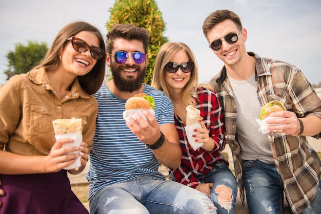 Przyjaciele siedzą w parku i jedzą fast foody.