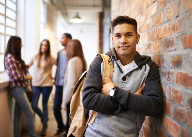 Przyjaciele sprawiają, że studia są zabawne Portret przystojnego młodego studenta opartego o ścianę z przyjaciółmi w tle