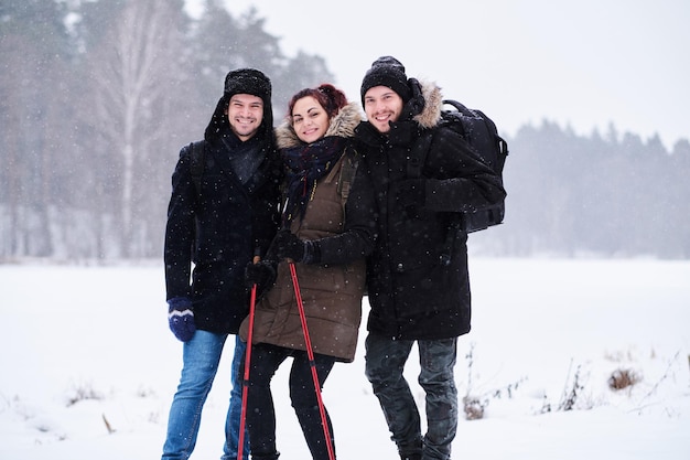 Przyjaciele wędrujący w zimnym, zaśnieżonym lesie stoją w uścisku i patrzą w kamerę.