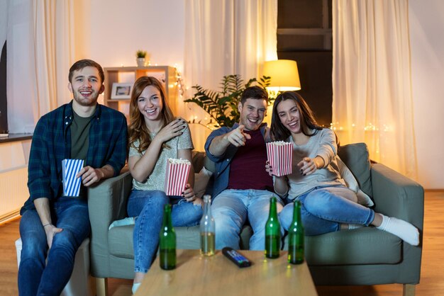 Przyjaciele z piwem i popcornem oglądają telewizję w domu.