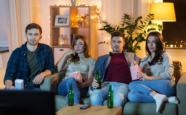 Przyjaciele z piwem i popcornem oglądają telewizję w domu.