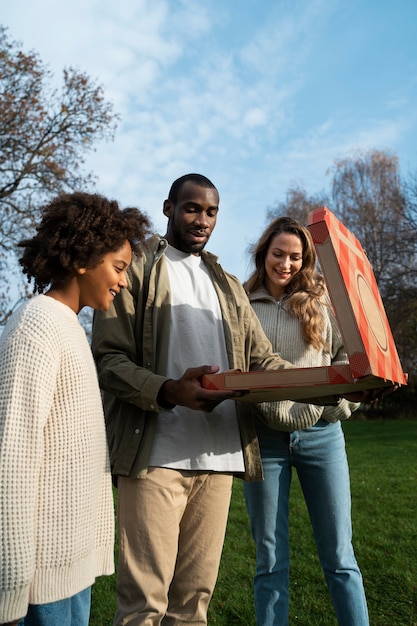 Przyjaciele z pizzą na zewnątrz widok z boku