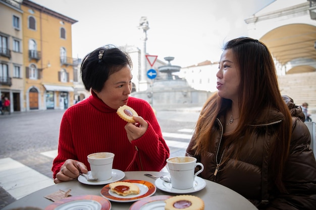 Przyjaciółki Chinek rozmawiają przy śniadaniu cappuccino i ciastkach w kawiarni