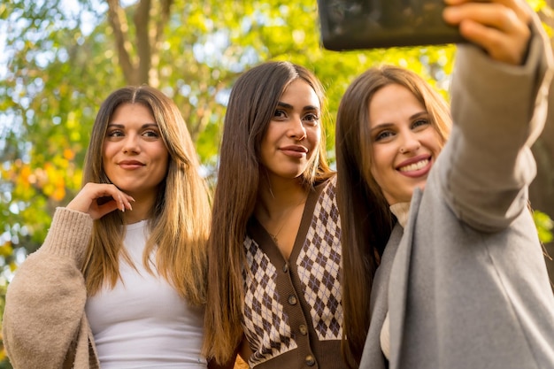 Przyjaciółki uśmiechające się w parku jesienią beztroskie robiące selfie jesienny styl życia