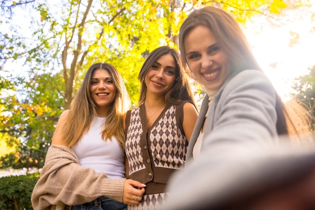 Przyjaciółki uśmiechające się w parku jesienią beztroskie robiące selfie jesienny styl życia