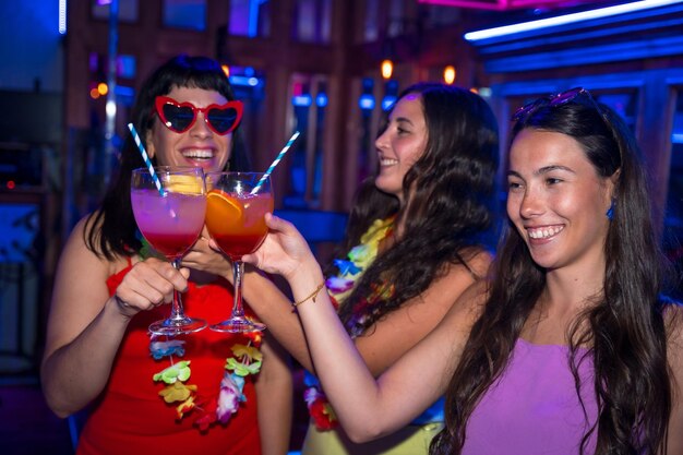 Zdjęcie przyjaciółki w nocnym klubie opiekają się i piją kieliszki alkoholu uśmiechając się na nocnej imprezie