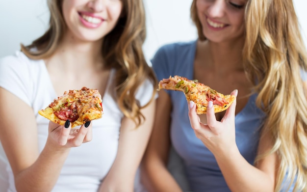 przyjaźń, ludzie, przyjęcie w piżamie i koncepcja fast foodów - zbliżenie szczęśliwych przyjaciół lub nastoletnich dziewcząt jedzących pizzę w domu