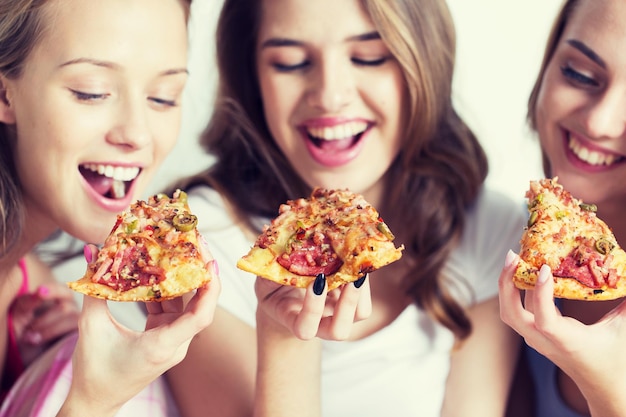 przyjaźń, ludzie, przyjęcie w piżamie i koncepcja fast foodów - zbliżenie szczęśliwych przyjaciół lub nastoletnich dziewcząt jedzących pizzę w domu