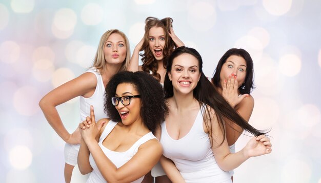 przyjaźń, piękno, pozytywne ciało i koncepcja ludzi - grupa szczęśliwych kobiet plus size w białej bieliźnie, bawiących się i robiących miny na świątecznym tle światła