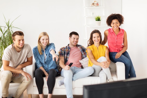 przyjaźń, rekreacja, śmieciowe jedzenie, ludzie i rozrywka koncepcja - szczęśliwi przyjaciele z zdalnym oglądaniem telewizji w domu