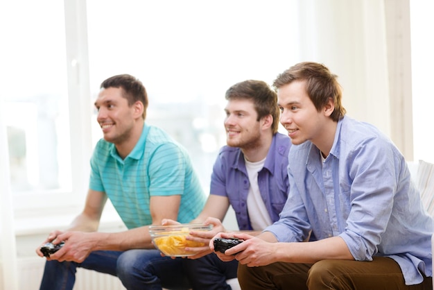 Zdjęcie przyjaźń, technologia, gry i koncepcja domu - uśmiechnięci koledzy grający w gry wideo w domu