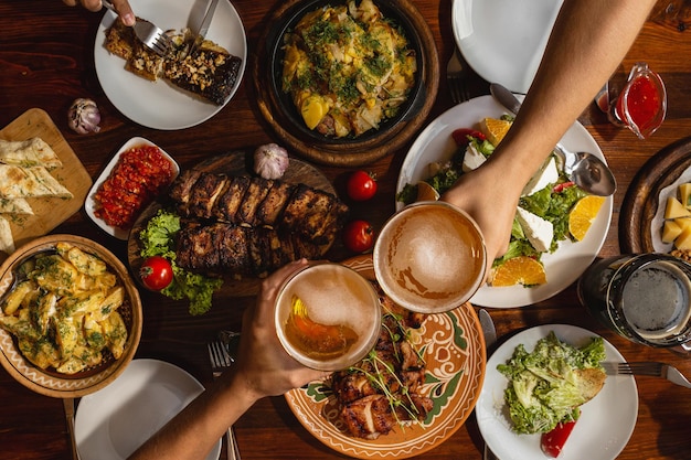 Przyjazna kolacja Widok z góry grupy ludzi jedzących razem kolację, siedząc przy rustykalnym drewnianym stole z wieloma talerzami pysznych i satysfakcjonujących posiłków