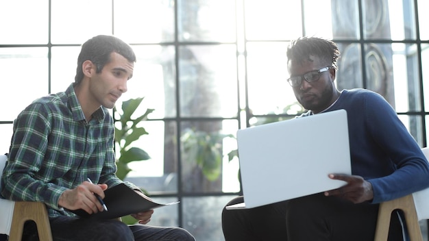 Przyjaźni koledzy rozmawiają siedząc w biurze obiecujący młody menedżer pokazuje prezentację na laptopie
