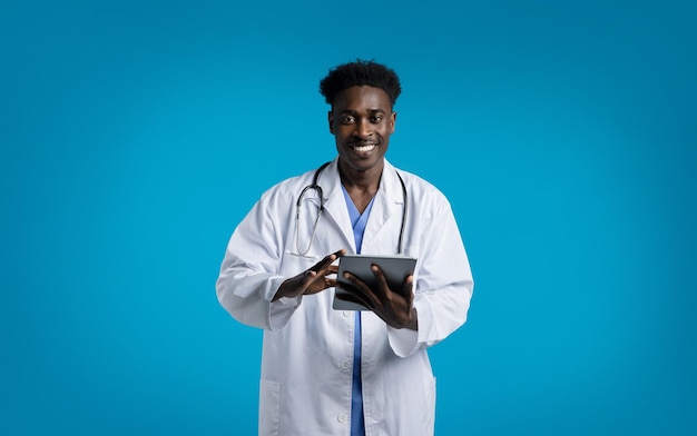 Przyjazny czarny lekarz trzymający cyfrową tabletkę na niebiesko
