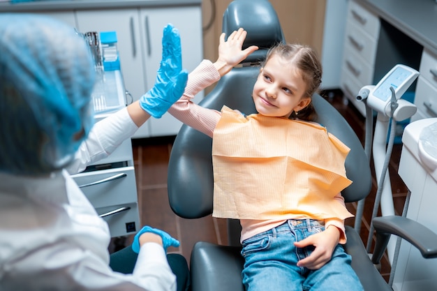 Przyjazny dentysta dający piątkę pacjentce siedzącej na fotelu dentystycznym po badaniu