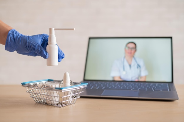 Przyjazny lekarz przeprowadza konsultację online na laptopie Farmaceuta w rękawiczkach wkłada lekarstwa do mini koszyka Koncepcja medycyny na odległość Zamawiaj leki online