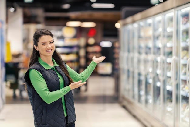 Przyjazny pracownik supermarketu pokazuje miejsce sprzedaży detalicznej i wita klientów