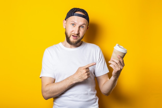 Przyjazny uśmiechnięty młody człowiek wskazuje palcem na papierowy kubek z kawą