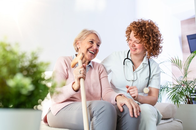 Przyjazny związek między uśmiechniętym opiekunem w mundurze i szczęśliwą starszą kobietą. Wspierająca młoda pielęgniarka patrzeje starszej kobiety.