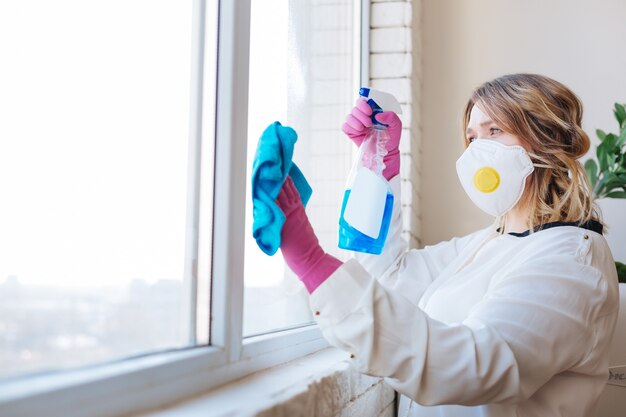 Przyjemna młoda kobieta w stroju ochronnym podczas mycia okien chemikaliami