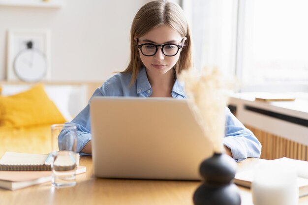 Przyjemna szczęśliwa młoda kobieta freelancer pracuje na komputerze w domu Atrakcyjna kobieta studiuje online za pomocą oprogramowania laptopa surfowanie po sieci informacje lub zakupy w sklepie internetowym