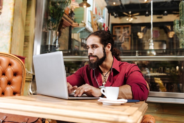 Przyjemny miły mężczyzna siedzący przed laptopem podczas pisania