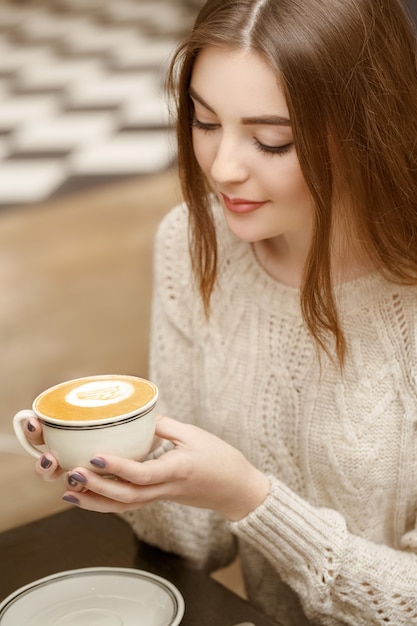 Przyjemny poranek. Pionowy portret pięknej brunetki przy filiżance kawy w kawiarni