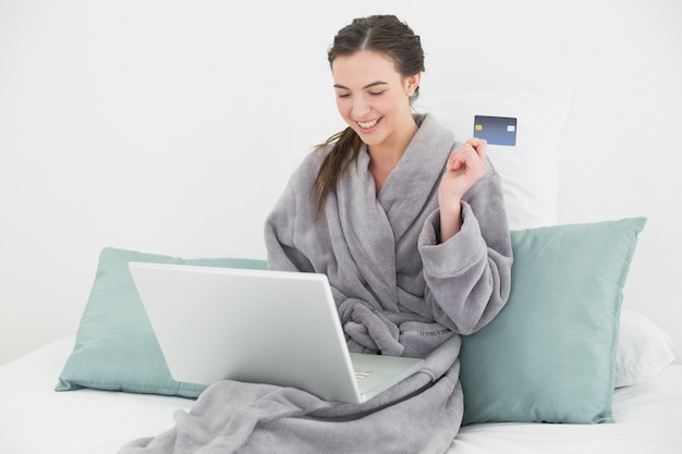 Przypadkowa kobieta w bathrobe robi online zakupy w łóżku