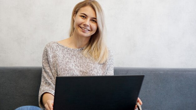 Przypadkowa młoda kobieta za pomocą laptopa w salonie w domu. Praca z domu w okresie kwarantanny