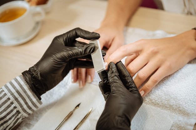 Przyrządy do manicure. Doświadczona stylistka paznokci w czarnych rękawiczkach przy pomocy instrumentów do manicure