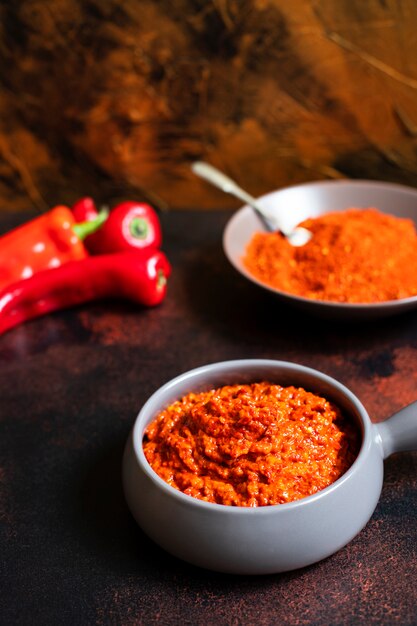 Przystawka Ajvar Balkan z pieczonej papryki. Kuchnia serbska i bałkańska. Ajvar w misce, papryka w proszku i świeża papryka w tle. Złoty bogaty kolor tła. Pionowy. Miejsce na tekst