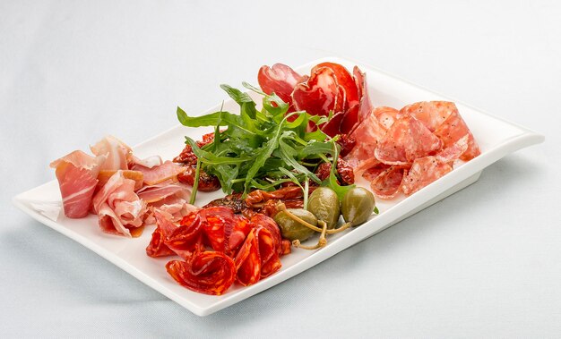 Przystawki z włoskich kiełbasek Prosciutto chorizo pancetta i salami kapary rukola i suszone pomidory na białym tle