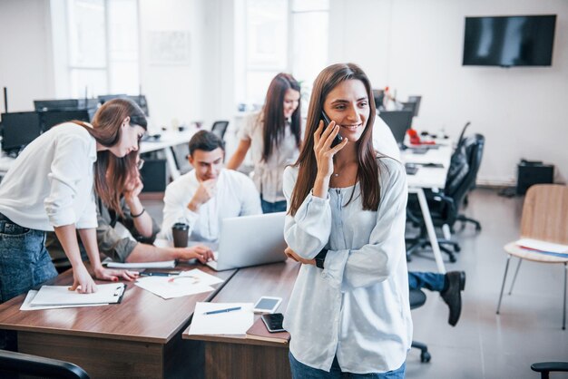 Przystojna kobieta z telefonem jest w biurze. Grupa osób pracujących przy projekcie za.